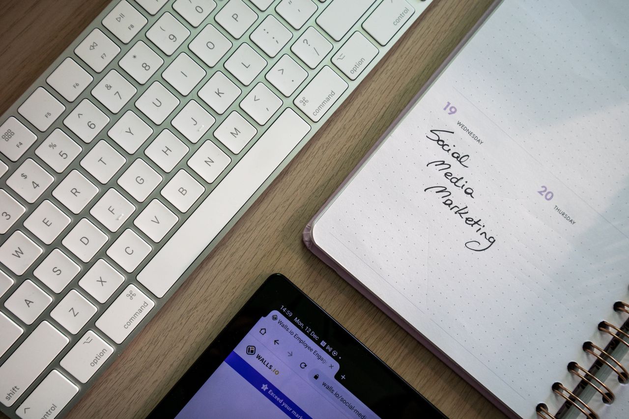 Vue de dessus d’un clavier, d’un agenda avec une note de marketing sur les réseaux sociaux, et d’une tablette posés sur un bureau.